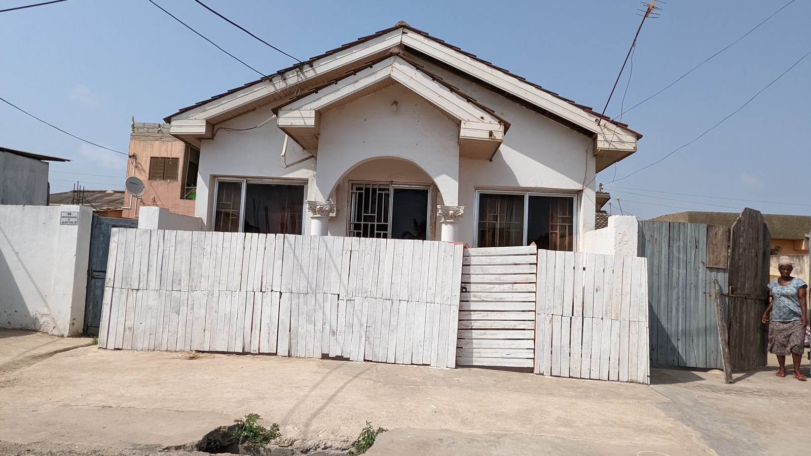 A single-storey house behind a white perimeter fence on a sandy plot