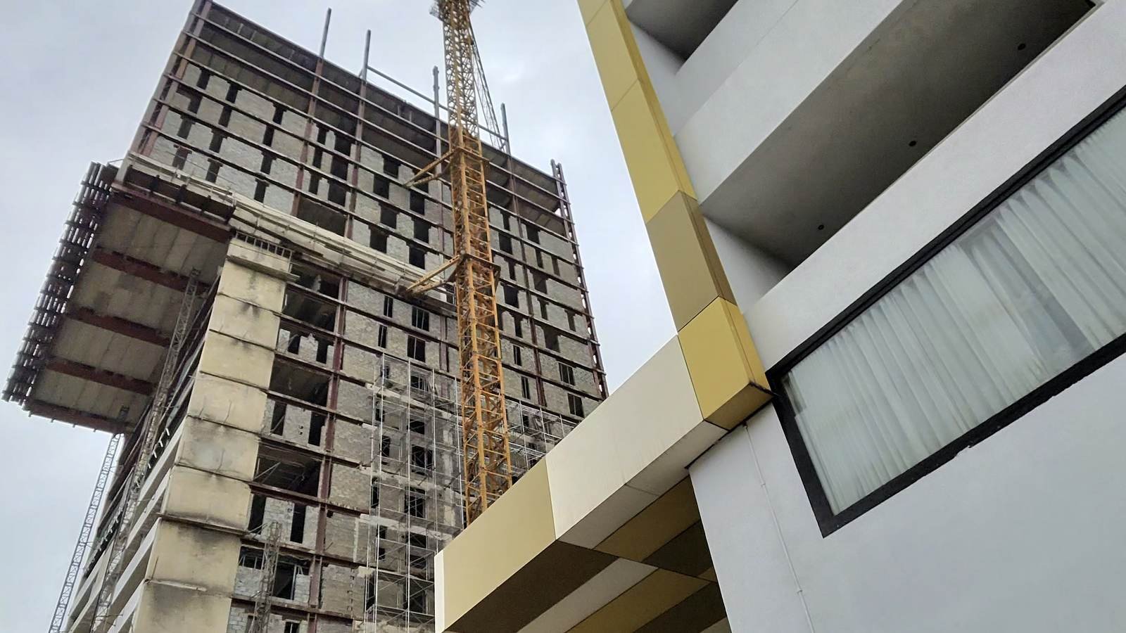 A tower crane working on a high-rise, framed by a finished building alongside